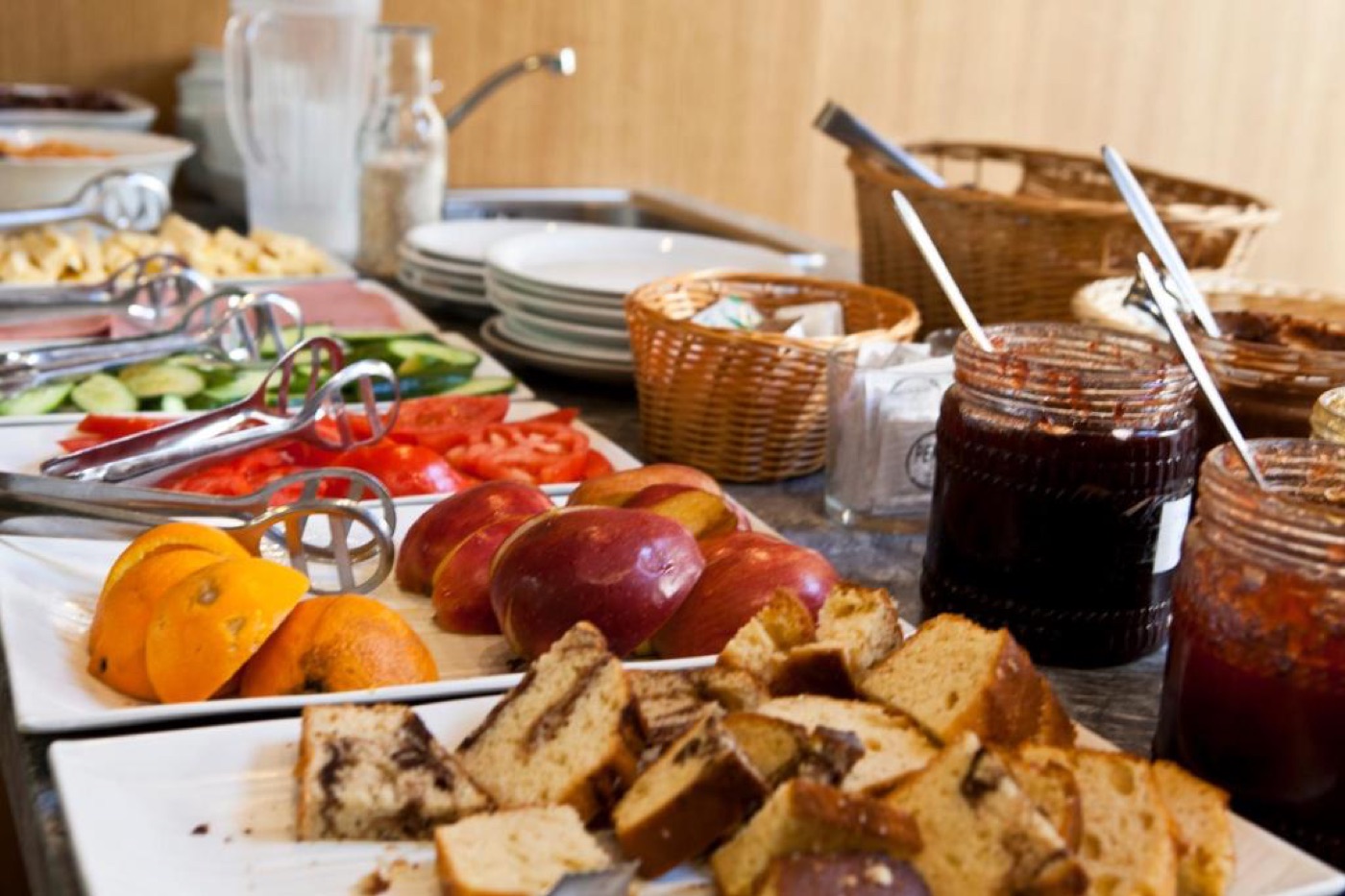A breakfast buffet with fruit, cake, cheese, vegetables and jam